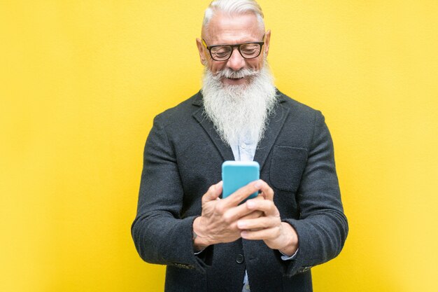 Homme senior branché à l'aide de l'application smartphone sur jaune