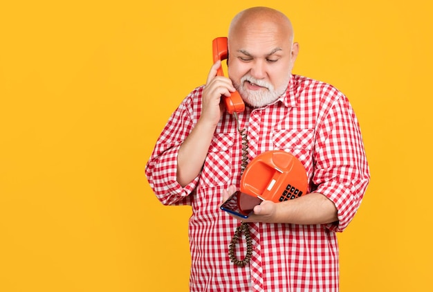 Homme senior confus avec téléphone rétro et smartphone moderne sur fond jaune