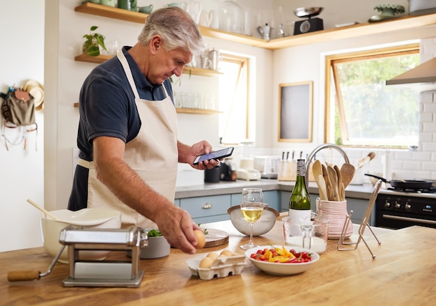 Homme senior cuisine et téléphone pour la recherche de recettes ou d'ingrédients pour le repas parfait dans la cuisine à la maison