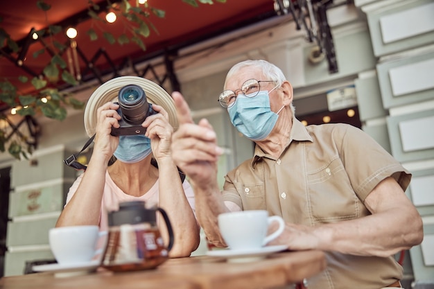 Homme senior dans un masque facial pointant vers quelque chose au loin vers une femme photographe