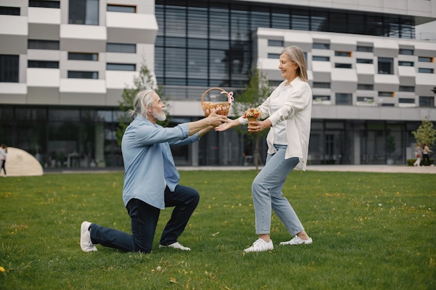 Homme senior debout sur une herbe en été et donner un panier de paille à une femme