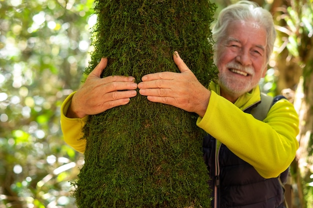 Homme senior défocalisé étreignant un tronc d'arbre recouvert de mousse dans les bois amour pour le plein air et la nature concept de jour de la terre Les gens sauvent la planète de la déforestation