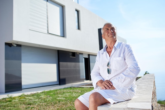 homme senior devant une villa de maison moderne de luxe