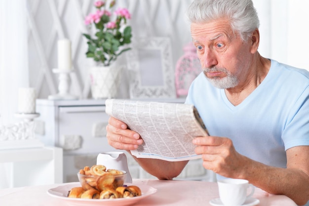 Homme senior émotionnel lisant le journal à la maison