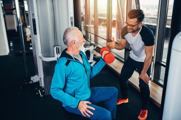 Homme senior exerçant dans une salle de sport avec son entraîneur personnel.