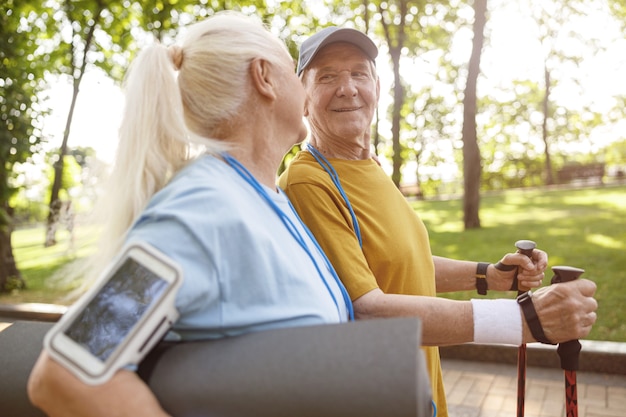 Photo homme senior gai avec des bâtons pour la marche nordique et femme dans un parc verdoyant