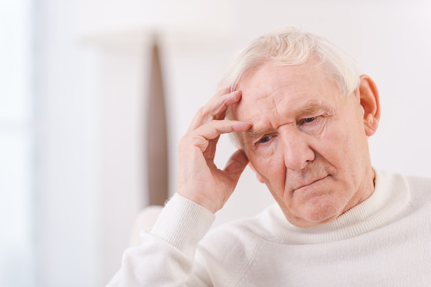 Homme senior inquiet. Homme senior frustré touchant sa tête alors qu'il était assis sur une chaise