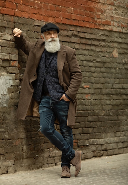 Homme senior à la mode avec des cheveux gris et une barbe est à l'extérieur dans la rue.