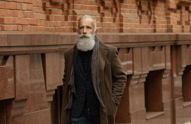 Homme senior à la mode avec des cheveux gris et une barbe est à l'extérieur dans la rue.