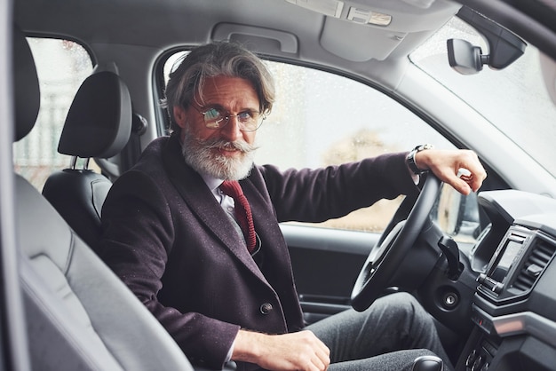 Un homme senior à la mode dans des vêtements élégants est dans la voiture moderne.