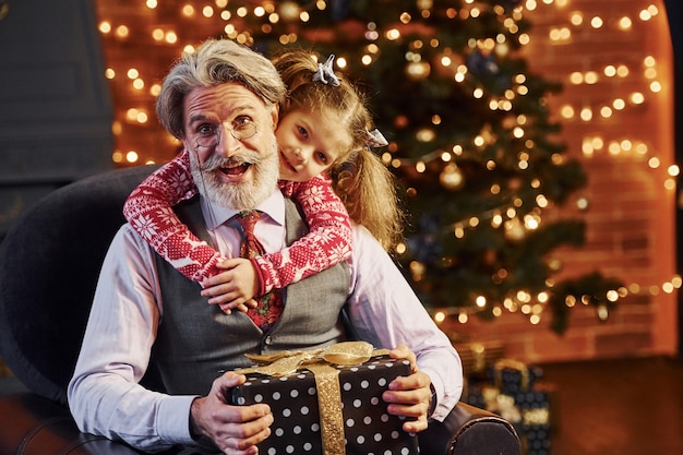 Homme senior à la mode gai aux cheveux gris et à la barbe avec une petite fille avec une boîte-cadeau s'embrassant.