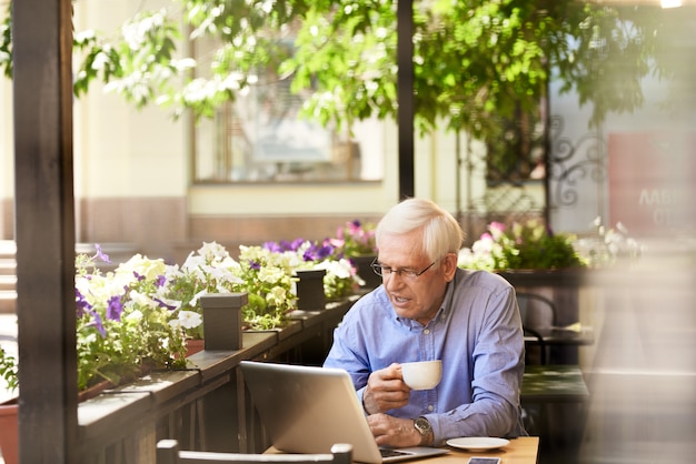 Homme senior moderne à l'aide d'un ordinateur portable dans un café à l'extérieur