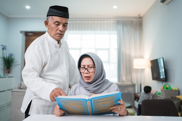 Homme senior musulman asiatique enseignant à sa femme la lecture du Coran ou du Coran dans le salon. couple musulman priant à la maison