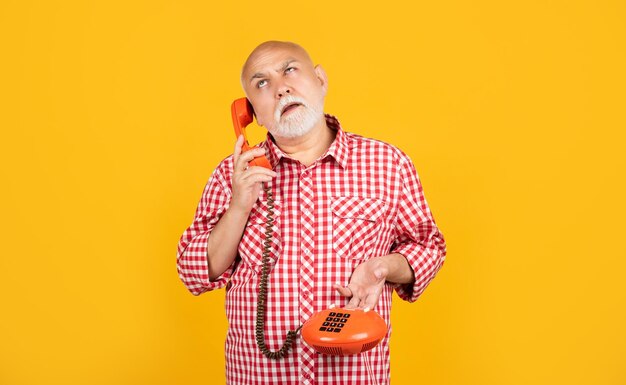 Homme senior pensant avec téléphone rétro sur fond jaune