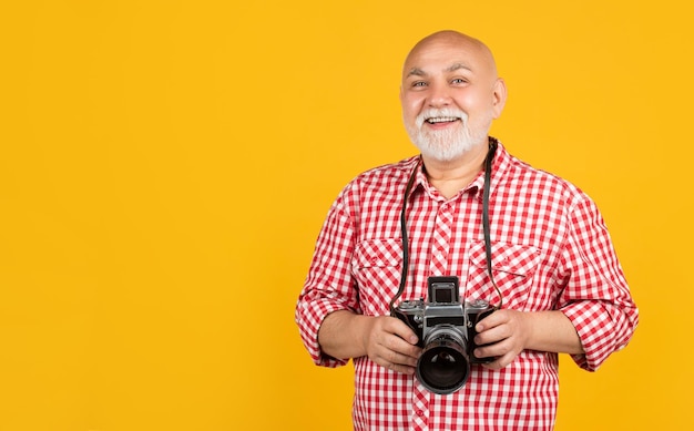 Homme senior souriant avec appareil photo rétro sur fond jaune