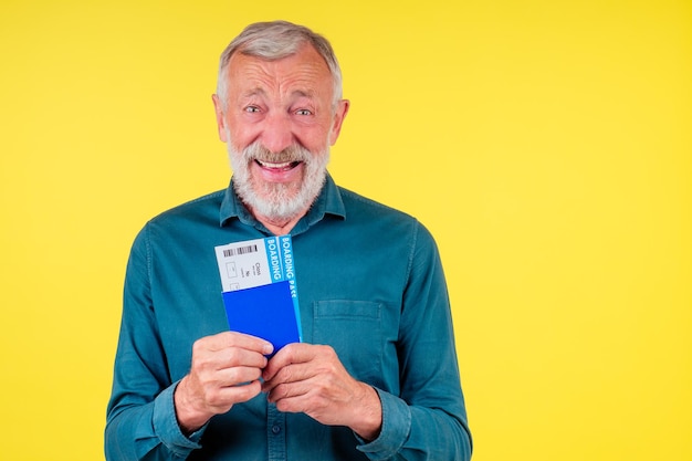 Homme senior souriant détenant un passeport dans une couverture bleue et des billets studio fond jaune.