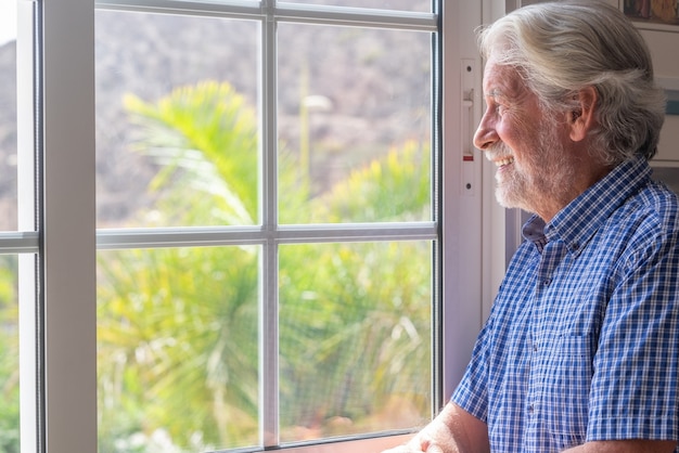 Homme senior souriant à la fenêtre regardant par