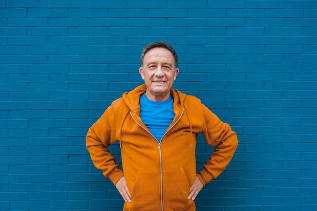 Un homme senior souriant posant devant un mur bleu