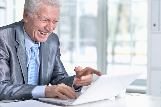 Homme senior en tenue de soirée à l'aide d'un ordinateur portable au bureau