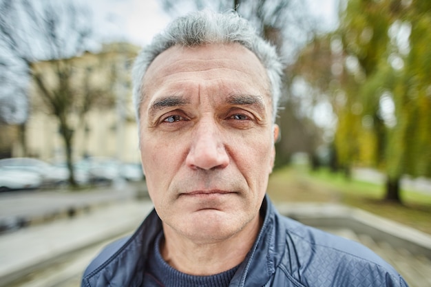 Un homme sérieux âgé est debout à l'extérieur.