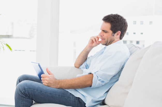 Homme sérieux assis sur le canapé avec sa tablette à la maison dans le salon