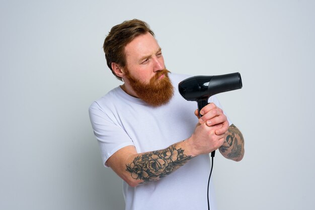 L'homme sérieux avec la barbe joue avec le sèche-cheveux comme arme de poing