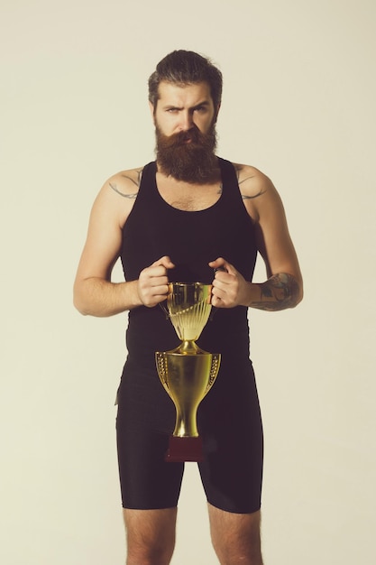 L'homme sérieux barbu tient la tasse de champion d'or sur le fond gris