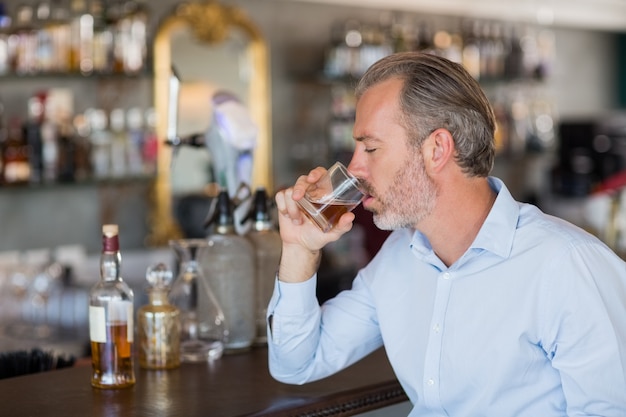 Homme sérieux, boire du whisky au comptoir du bar