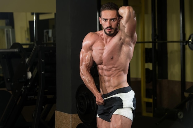 Homme sérieux debout fort dans la salle de gym et muscles fléchissants