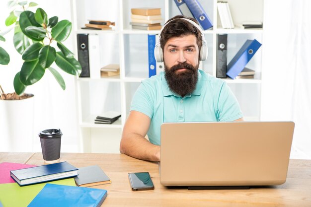 Homme sérieux écoutant un webinaire dans un casque à l'aide d'un ordinateur portable dans l'éducation en ligne de bureau