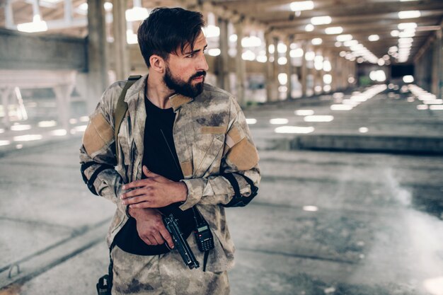 Un homme sérieux est debout dans un hangar et tient un pistolet de paintball dans les mains.