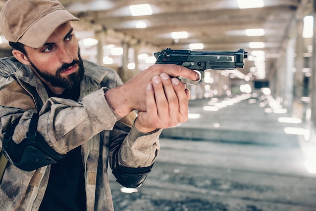 Un homme sérieux est debout dans un hangar et tient un pistolet de paintball dans les mains.
