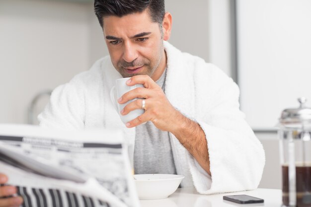 Homme sérieux avec une tasse de café en lisant le journal dans la cuisine