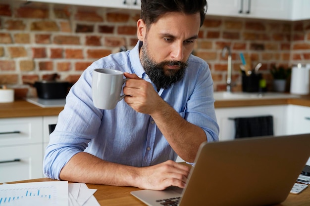 Un homme sérieux tenant une tasse de café et travaillant à la maison.