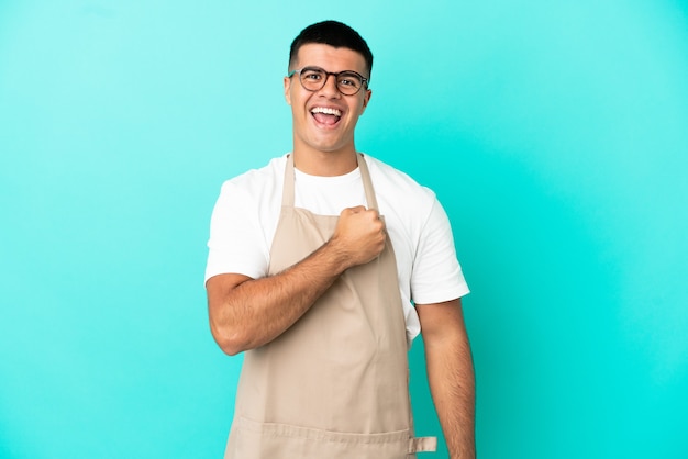 Homme de serveur de restaurant sur fond bleu isolé célébrant une victoire