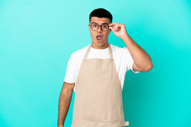 Homme de serveur de restaurant sur fond bleu isolé avec des lunettes et surpris