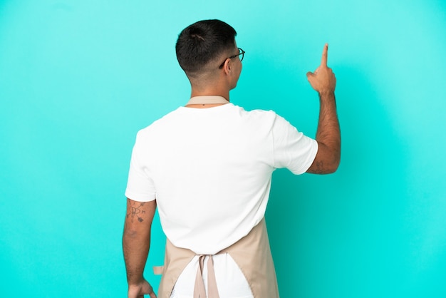 Homme de serveur de restaurant sur fond bleu isolé pointant vers l'arrière avec l'index