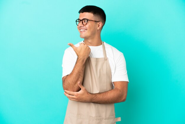 Homme de serveur de restaurant sur fond bleu isolé pointant vers le côté pour présenter un produit