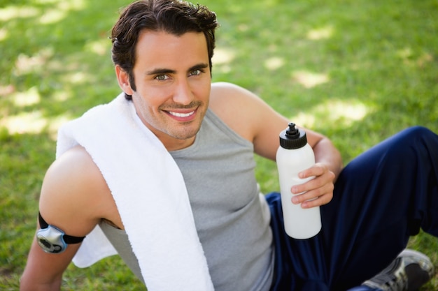 Homme avec une serviette sur son épaule regardant vers le haut tout en tenant une bouteille de sport