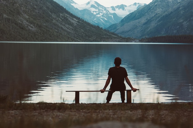 Un homme seul assis sur le banc devant le lac. Le touriste apprécie de belles vues de lac de montagne le soir