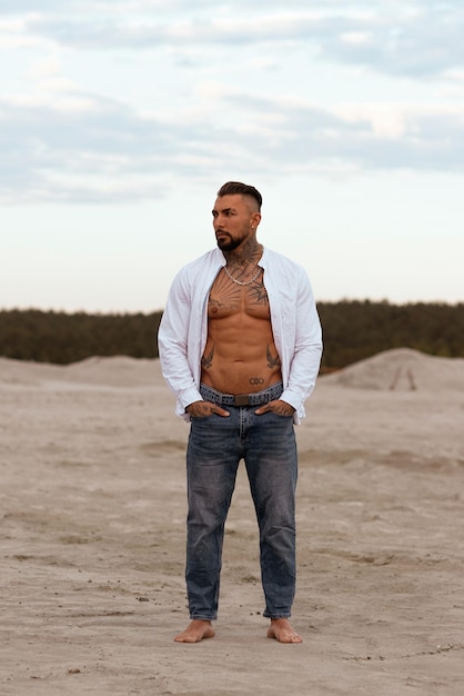 Homme sexy athlétique musclé en chemise blanche avec torse nu repose sur la plage