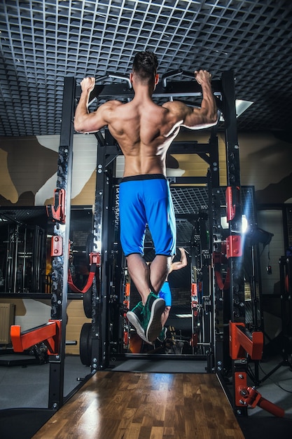 Homme sexy dans la salle de gym avec des haltères. Un homme sportif avec de gros muscles et un dos large s'entraîne dans la salle de gym, le fitness et la presse abdominale gonflée. Russie, Sverdlovsk, 2 juin 2018