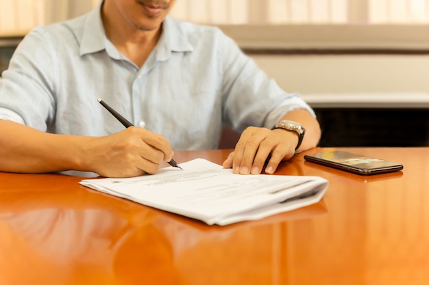 Homme signature de documents avec plume sur un bureau en bois.