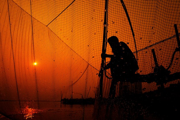 L'homme en silhouette contre le ciel orange vu à travers la clôture au coucher du soleil