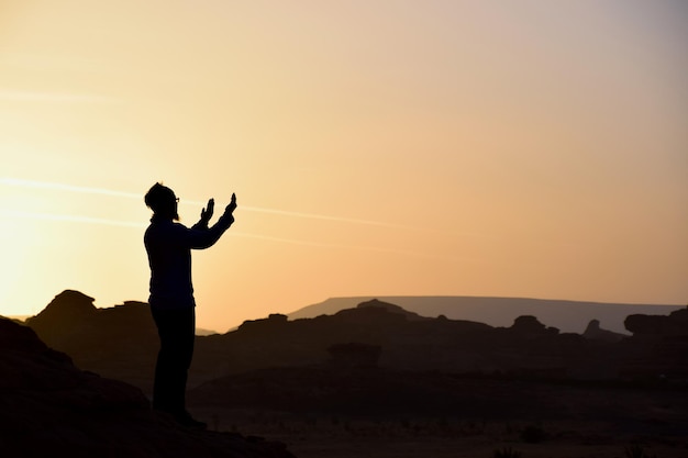 L'homme en silhouette debout sur la montagne contre le ciel au coucher du soleil
