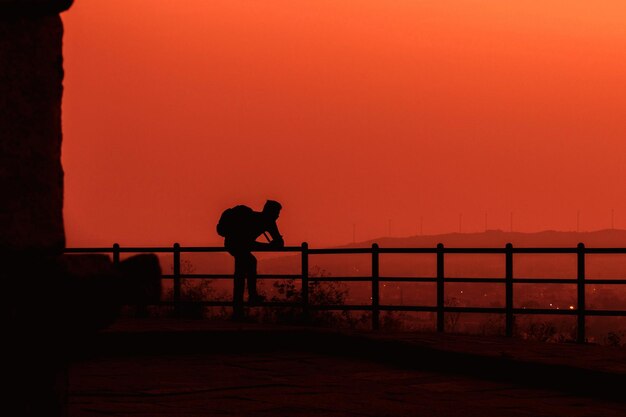 Photo homme de silhouette debout près de la balustrade contre la vue sur la colline au coucher du soleil