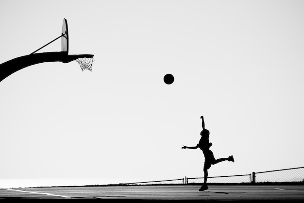 Un homme en silhouette jouant au basket sur le terrain contre un ciel clair