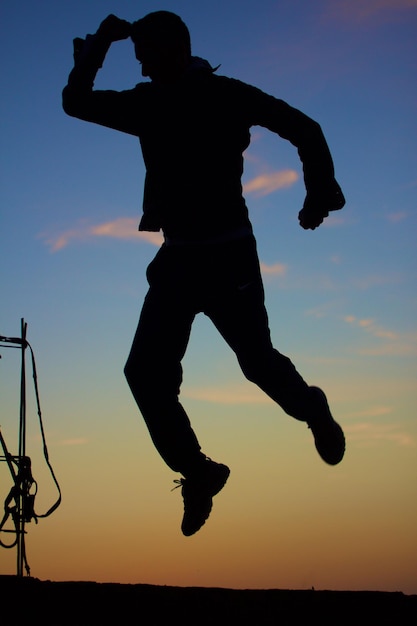 Un homme à la silhouette ludique sautant contre le ciel au coucher du soleil