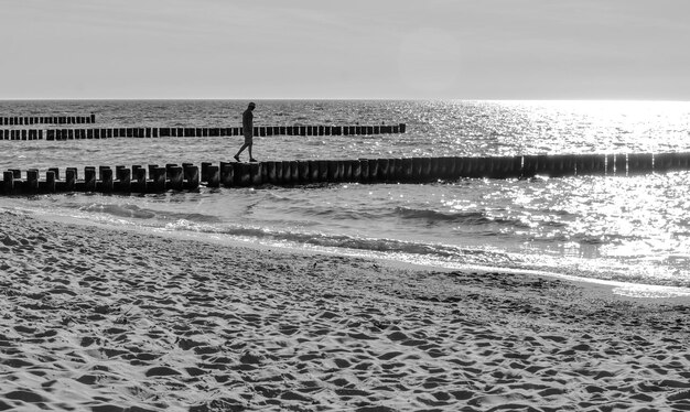 Photo un homme en silhouette marchant sur un poteau de bois sur la plage contre le ciel