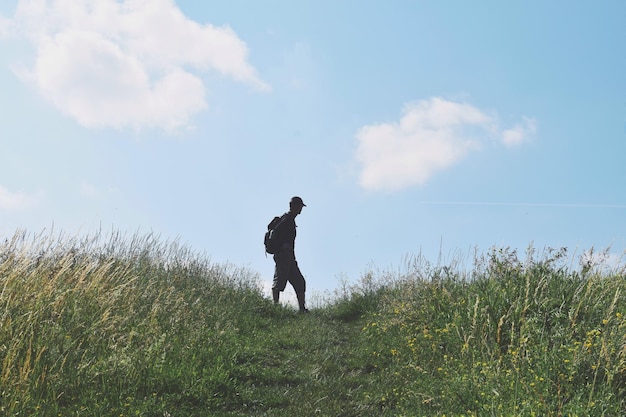 Un homme en silhouette marchant sur une terre herbeuse contre le ciel